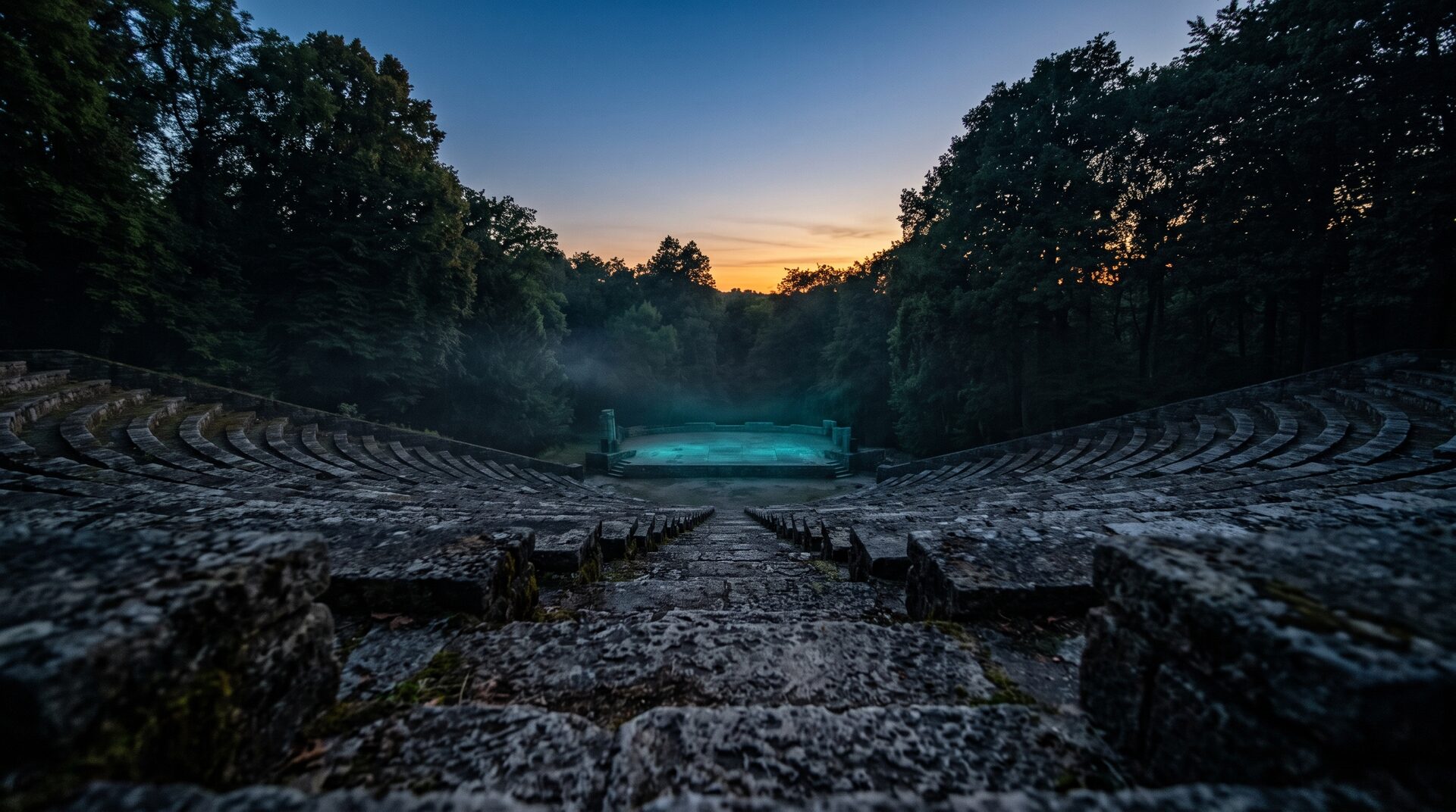 The amphitheatre's symmetric stone steps descending toward a teal-lit stage at blue hour
